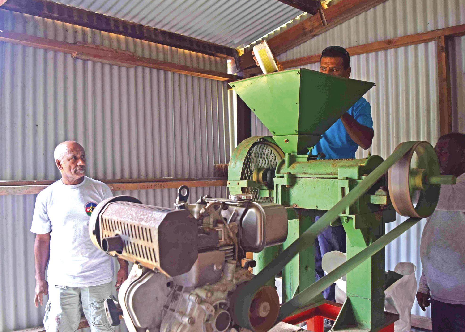 Pierre Cottin (à gauche), est le fil de Jean Ounou-Cottin, qui a relancé la culture du café  à Bangou. Ici, il montre la machine qui permet de broyer les grains avant la torréfaction.