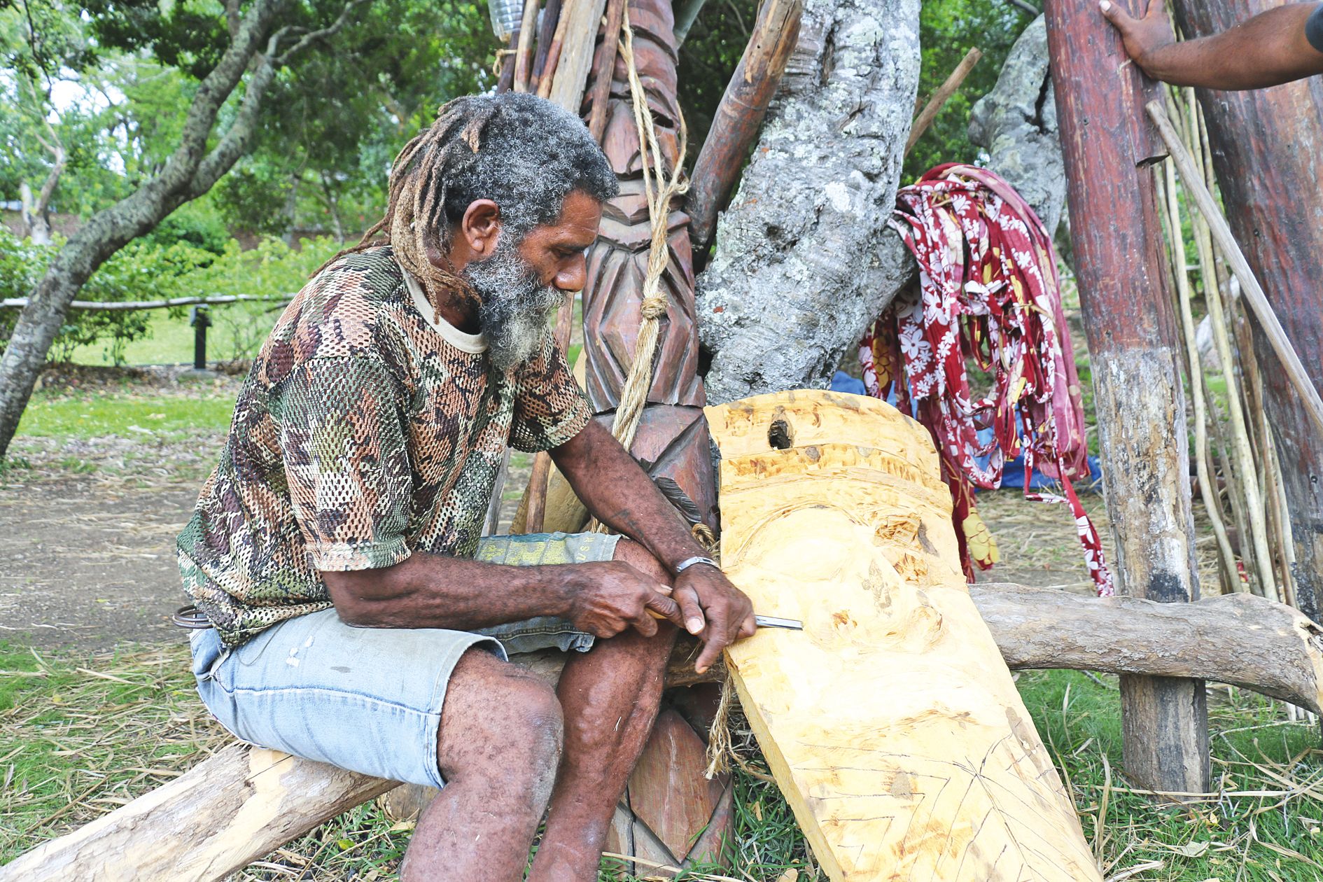 Pendant la pause, Pwêdé, sculpteur à ses heures, travaille à la décoration du faré qui sera accrochée sur les poteaux.