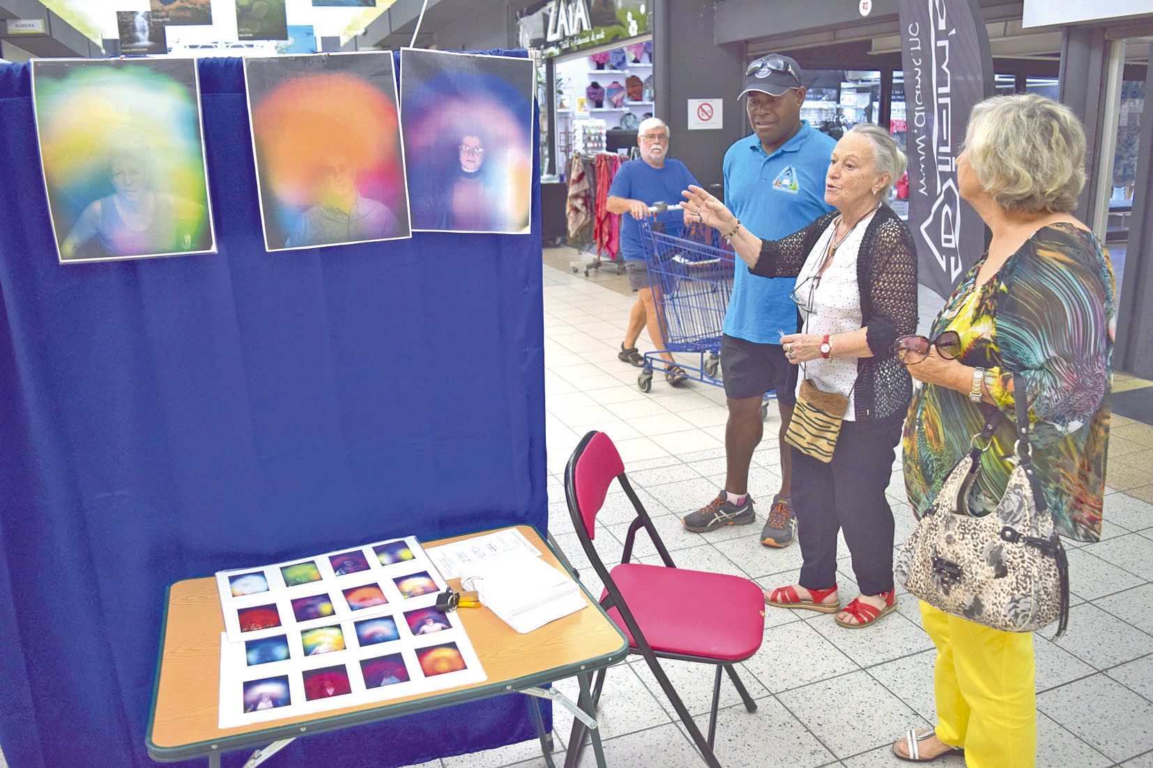 Lax Wéjième, pasteur, s’est arrêté sur le stand des photos d’aura de Madeleine, par curiosité. Ange-Line, l’organisatrice du festival au premier plan.