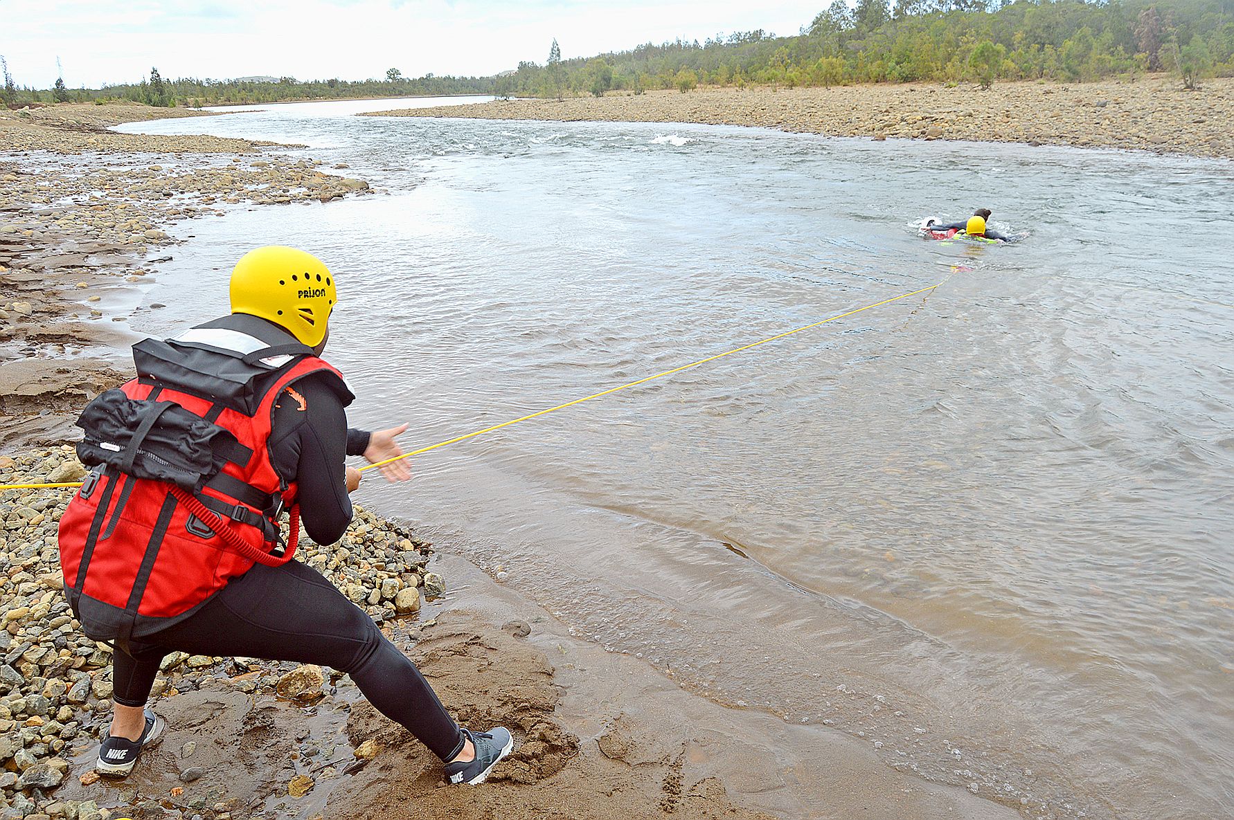 Un équipier, placé le long de la berge, a envoyé sa corde  au pompier nageur et le tire avec la victime hors de l’eau.